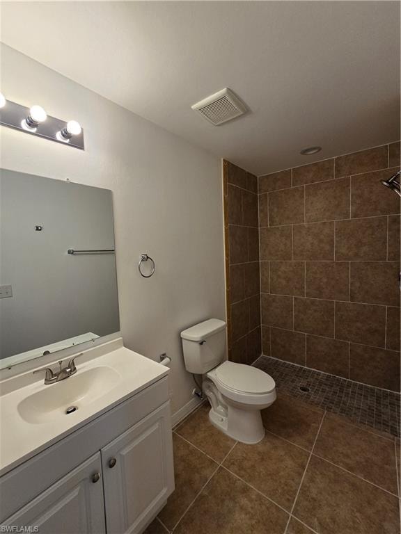 Bathroom with tiled shower, vanity, and dark tile patterned floors