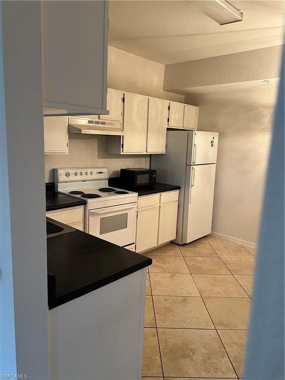 Kitchen with range, white cabinets, a textured wall, white fridge, and light tile patterned floors