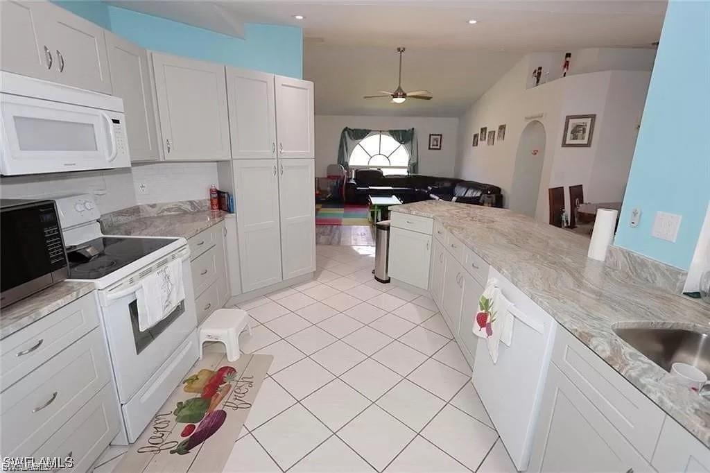 Kitchen featuring lofted ceiling, white appliances, white cabinets, open floor plan, and a ceiling fan