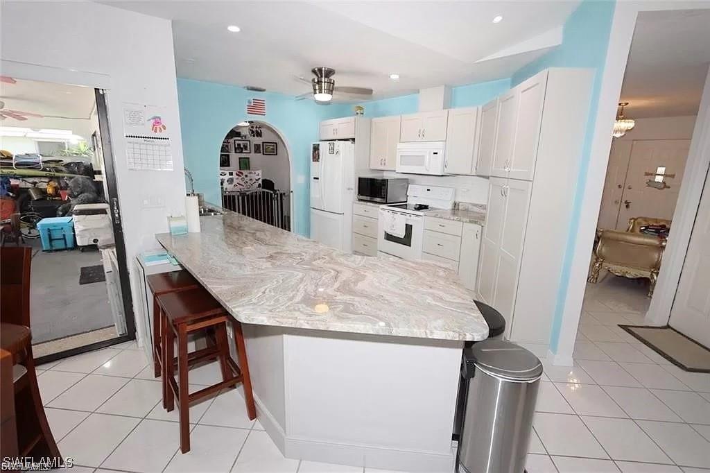 Kitchen with a ceiling fan, white appliances, a kitchen bar, white cabinetry, and recessed lighting