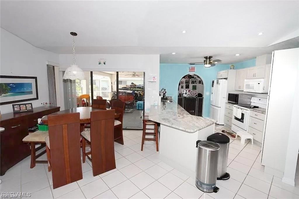 Kitchen with pendant lighting, white cabinetry, white appliances, light stone countertops, and a kitchen bar