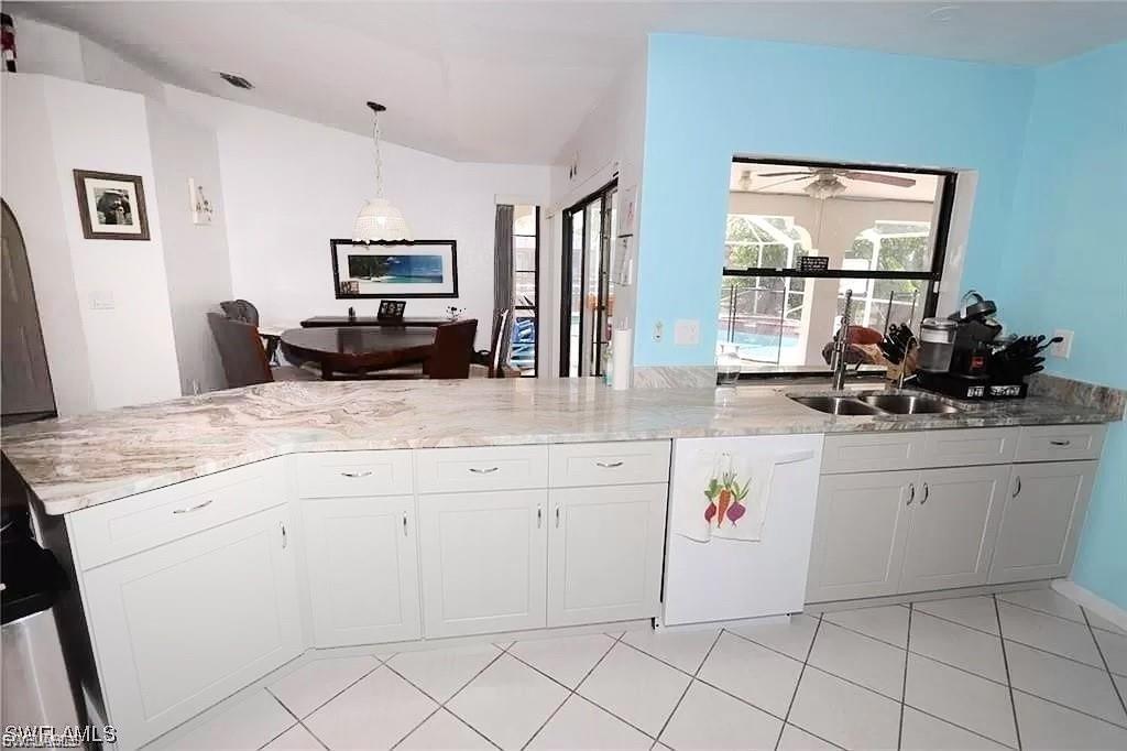 Kitchen with decorative light fixtures, a peninsula, dishwasher, white cabinetry, and light stone countertops
