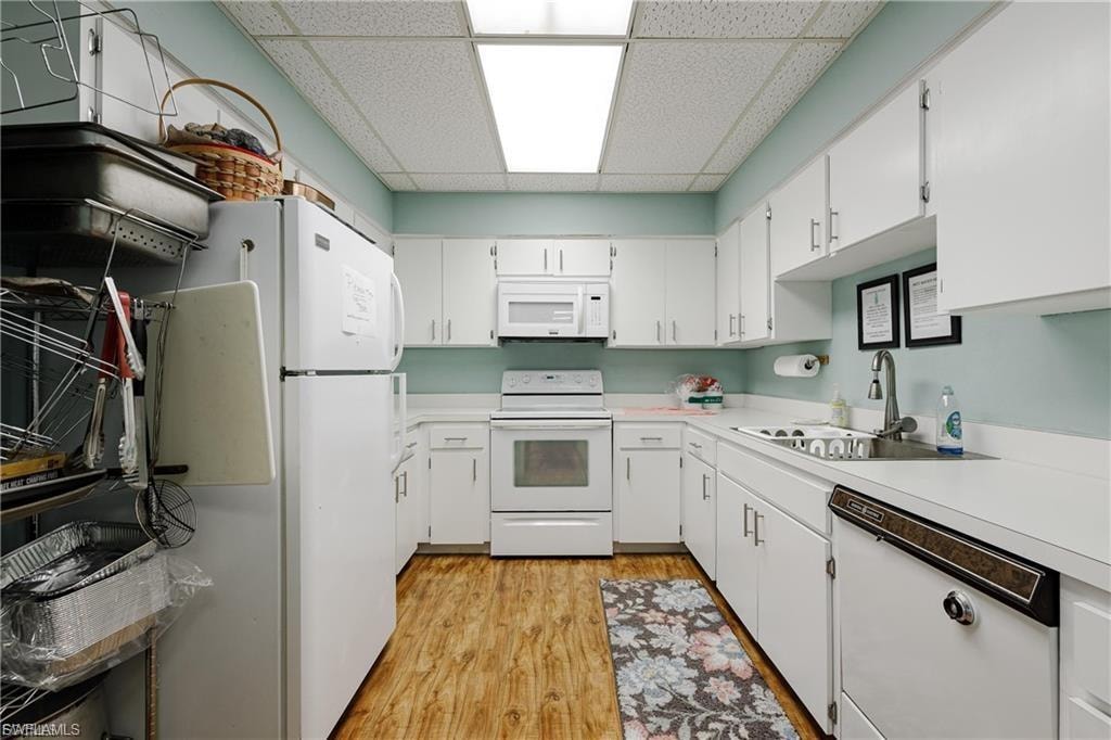 Kitchen with a paneled ceiling, white appliances, white cabinetry, light countertops, and light wood-style flooring