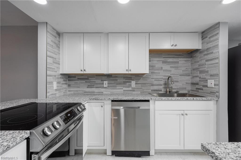 Kitchen with appliances with stainless steel finishes, white cabinetry, light stone counters, decorative backsplash, and recessed lighting