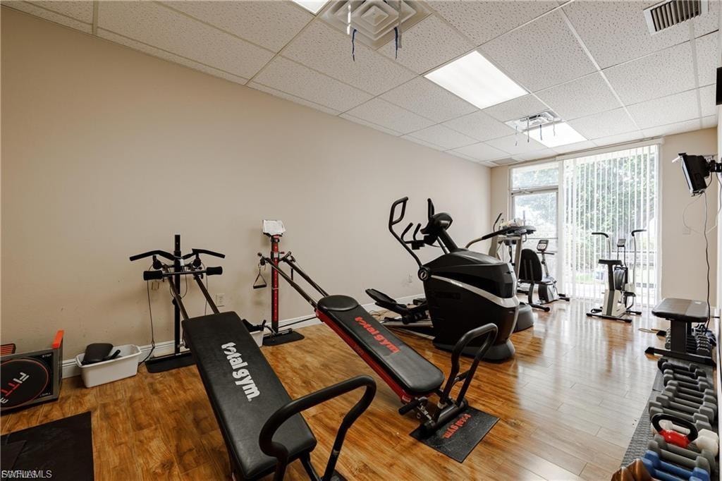 Gym featuring a paneled ceiling, a wall of windows, and wood finished floors