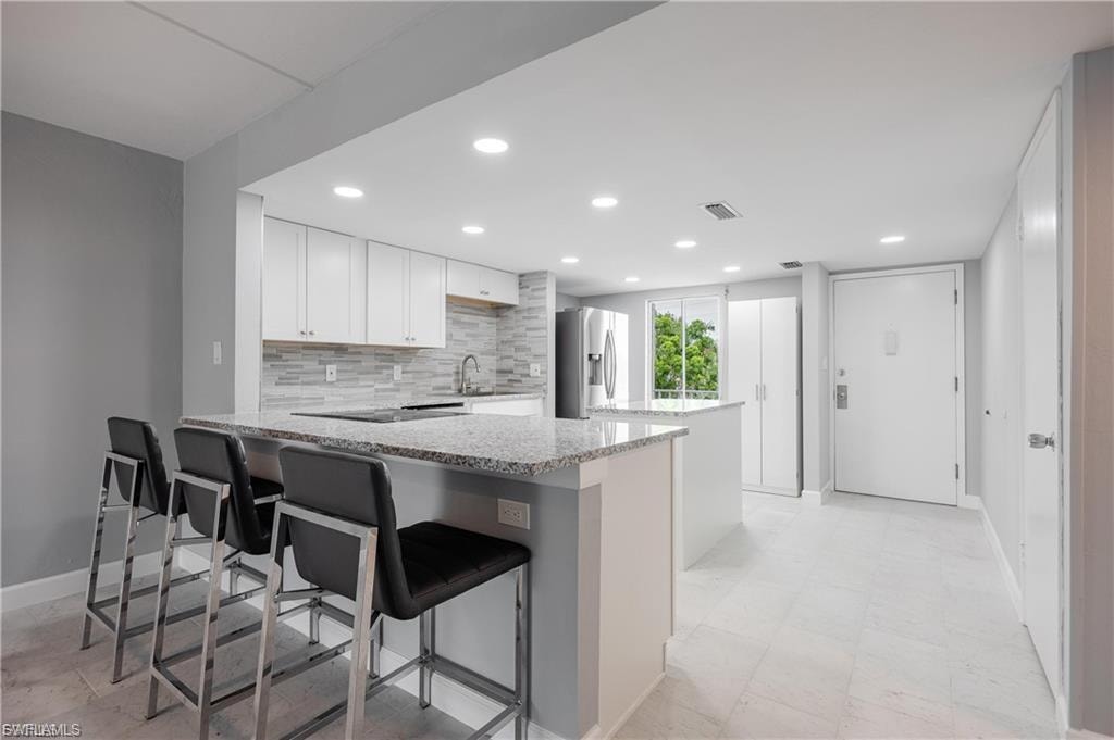 Kitchen with a peninsula, white cabinetry, a breakfast bar, stainless steel fridge, and tasteful backsplash