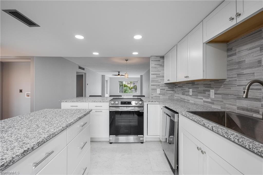 Kitchen with white cabinets, stainless steel appliances, a peninsula, decorative backsplash, and light stone countertops