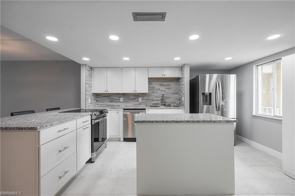 Kitchen with appliances with stainless steel finishes, white cabinetry, a kitchen island, a peninsula, and light stone countertops