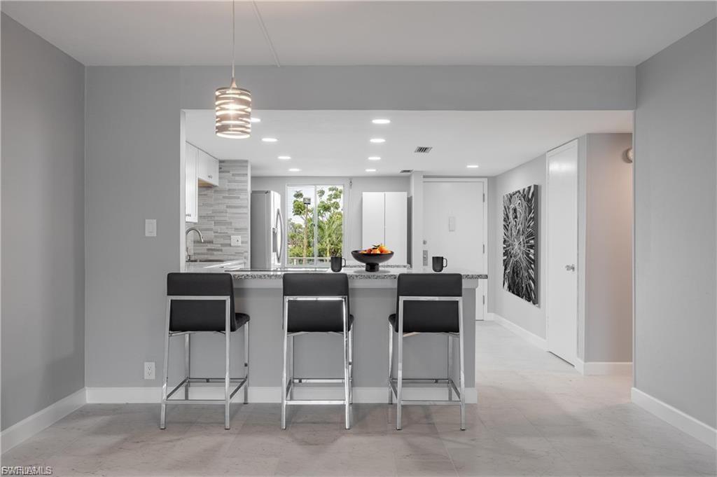 Kitchen featuring a peninsula, light stone counters, a breakfast bar area, freestanding refrigerator, and white cabinetry