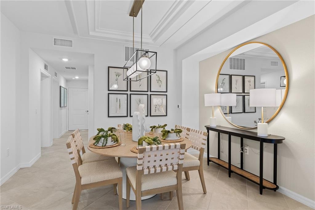 Dining area featuring a tray ceiling, ornamental molding, and light tile patterned flooring