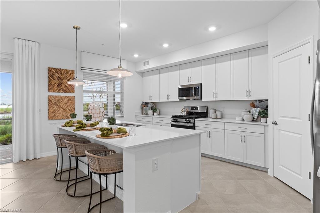 Kitchen with stainless steel appliances, a kitchen island with sink, a breakfast bar, white cabinets, and recessed lighting