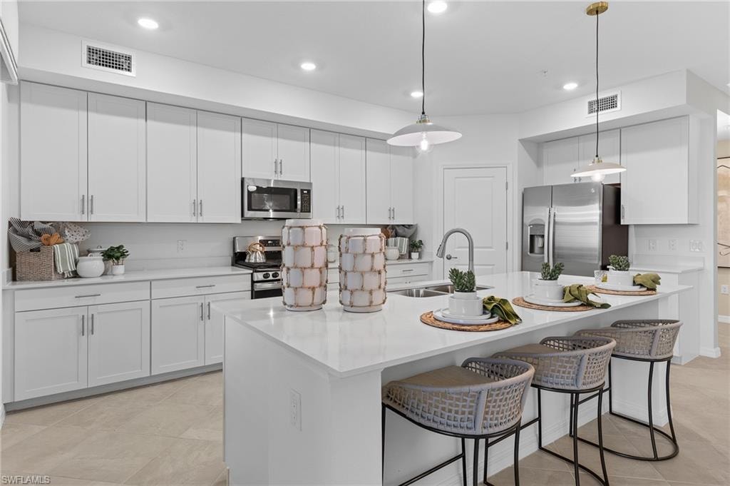 Kitchen with a breakfast bar area, decorative light fixtures, appliances with stainless steel finishes, white cabinets, and recessed lighting