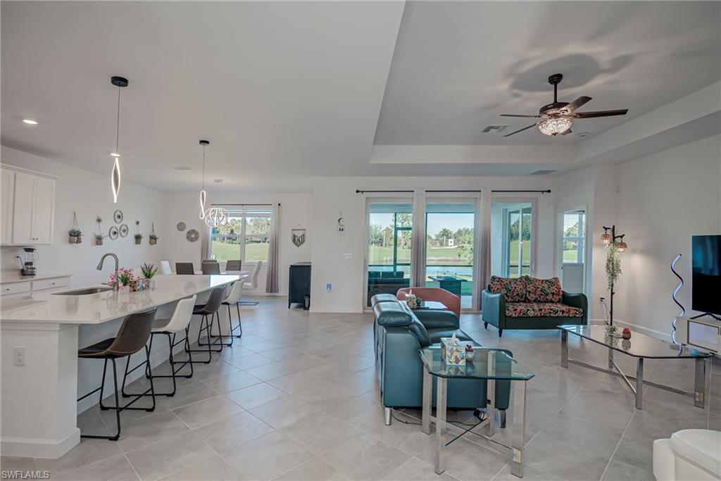 Living room featuring a tray ceiling, light tile patterned flooring, and a ceiling fan