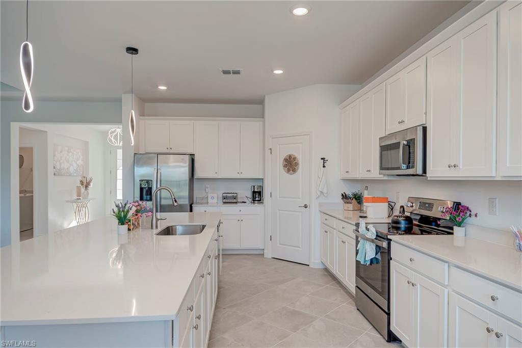 Kitchen featuring stainless steel appliances, white cabinetry, hanging light fixtures, a center island with sink, and light stone countertops
