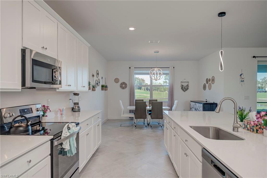 Kitchen with appliances with stainless steel finishes, white cabinets, decorative light fixtures, light stone counters, and recessed lighting