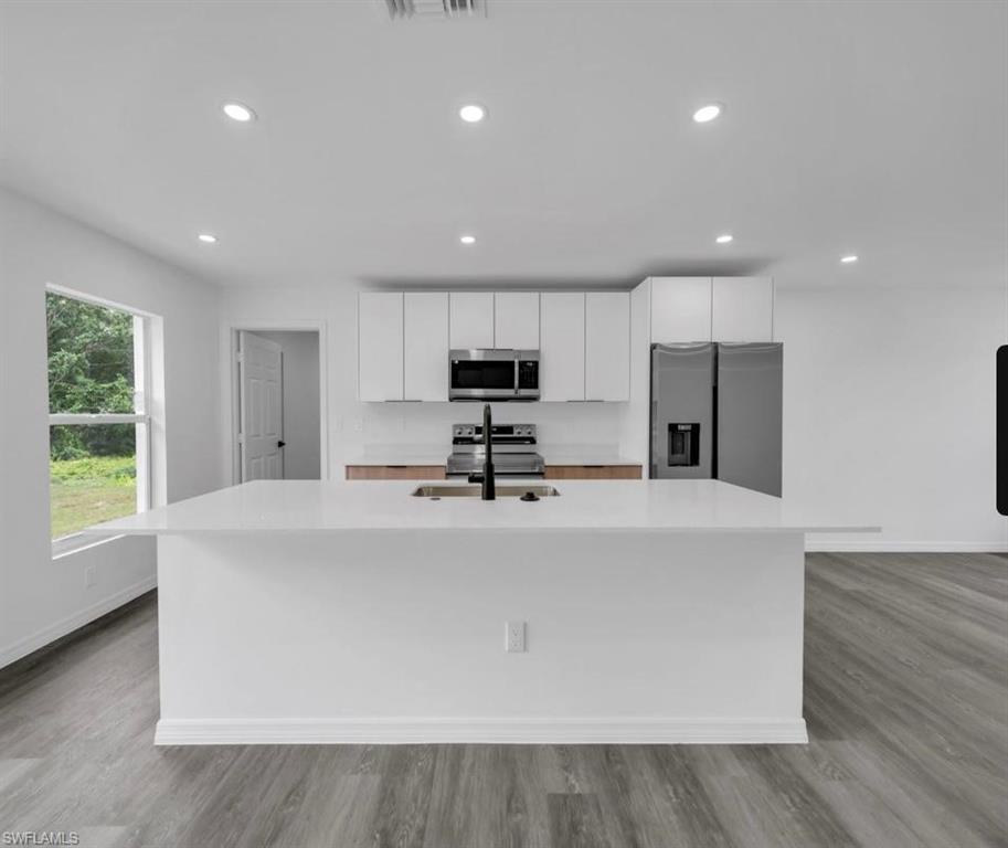 Kitchen featuring an island with sink, stainless steel appliances, white cabinetry, recessed lighting, and light wood-style flooring