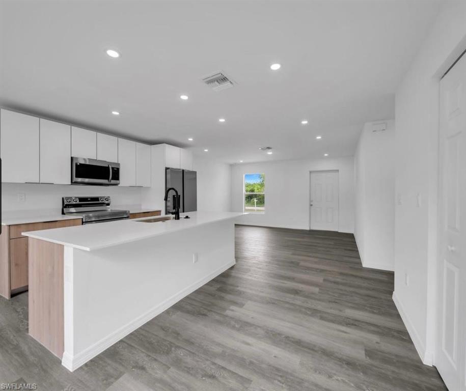 Kitchen featuring white cabinets, an island with sink, recessed lighting, appliances with stainless steel finishes, and open floor plan