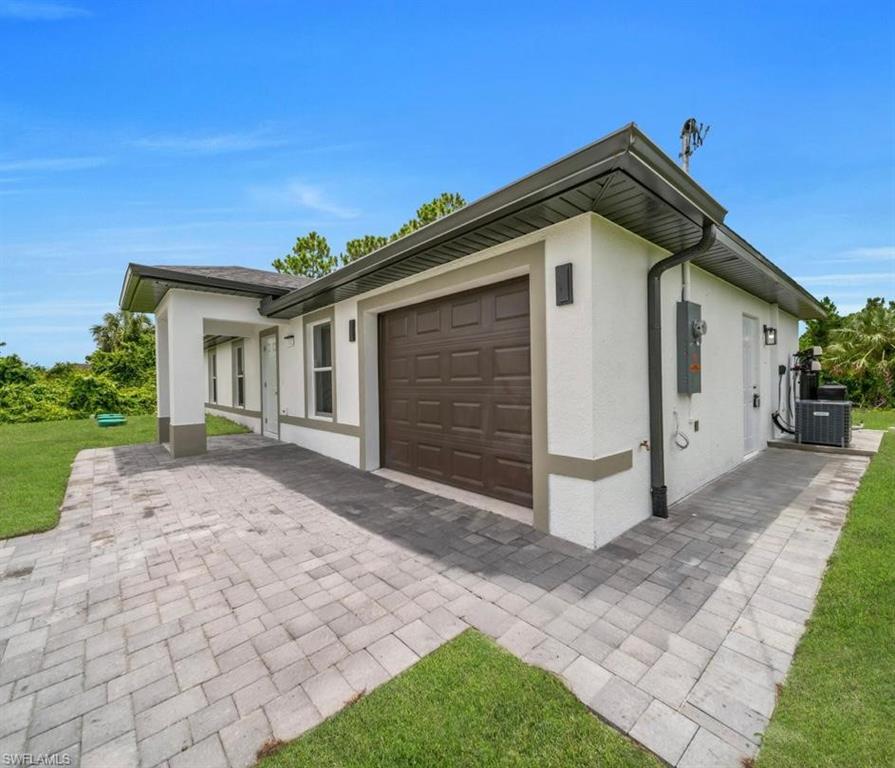 View of home's exterior featuring stucco siding, a garage, a lawn, and decorative driveway