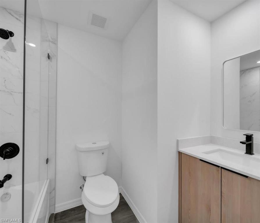 Full bath featuring vanity, a combined bath / shower with marble appearance, and dark wood-style floors