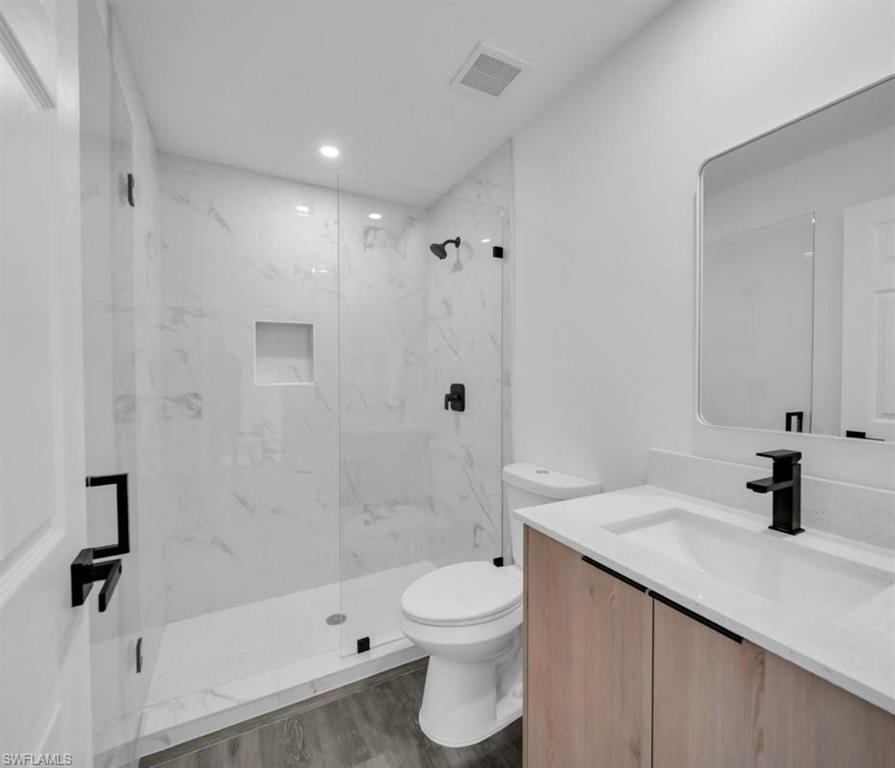 Full bath with vanity, a marble finish shower, and dark wood-style floors