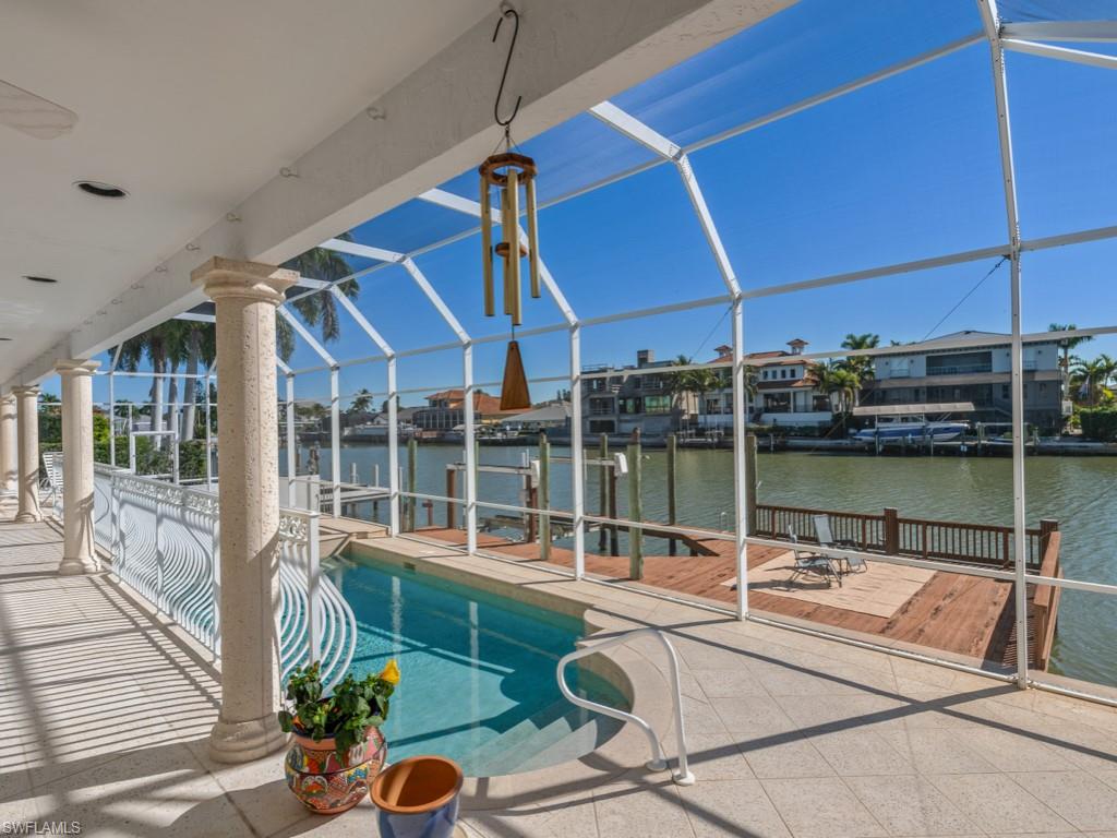 Swimming pool with a dock, glass enclosure, a sunroom, a water view, and a patio area