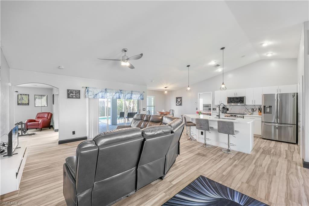 Living area with lofted ceiling, light wood-style floors, arched walkways, and a ceiling fan
