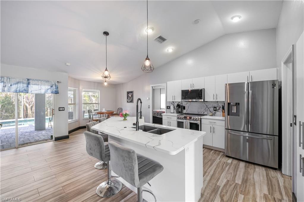Kitchen with appliances with stainless steel finishes, decorative light fixtures, backsplash, a kitchen bar, and a kitchen island with sink