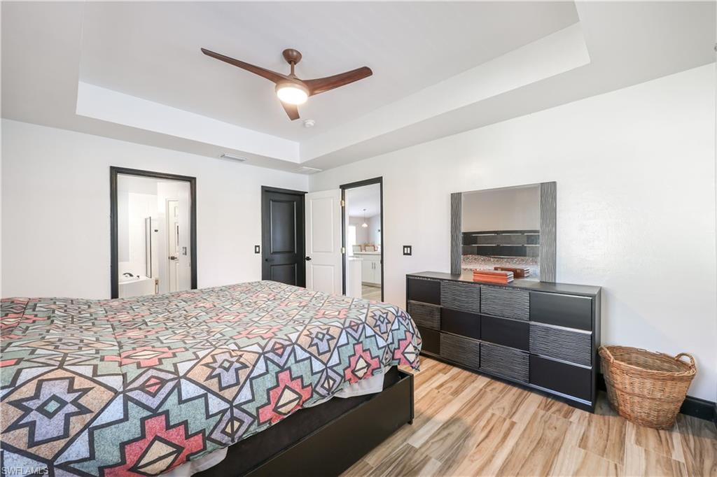 Bedroom featuring a tray ceiling, connected bathroom, wood finished floors, and ceiling fan
