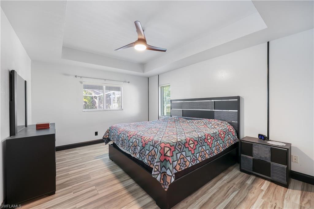 Bedroom with a raised ceiling, a ceiling fan, and light wood finished floors