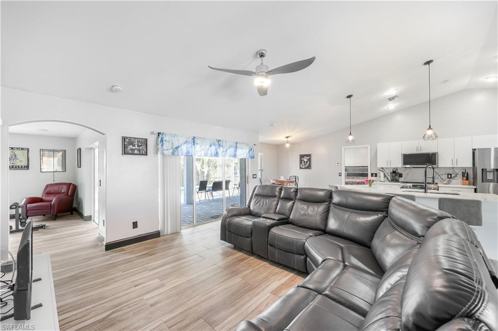Living area with lofted ceiling, light wood-type flooring, arched walkways, and a ceiling fan