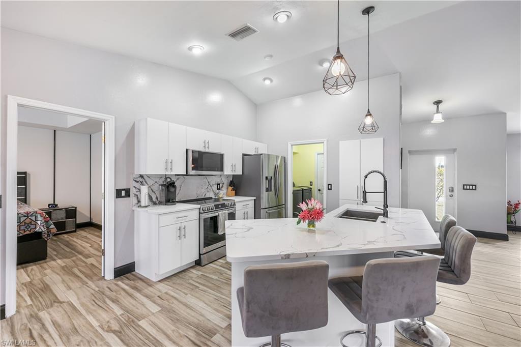 Kitchen featuring a kitchen bar, stainless steel appliances, pendant lighting, backsplash, and white cabinetry