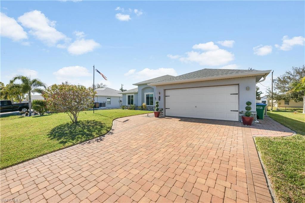 Ranch-style home with a front lawn, decorative driveway, stucco siding, and a garage