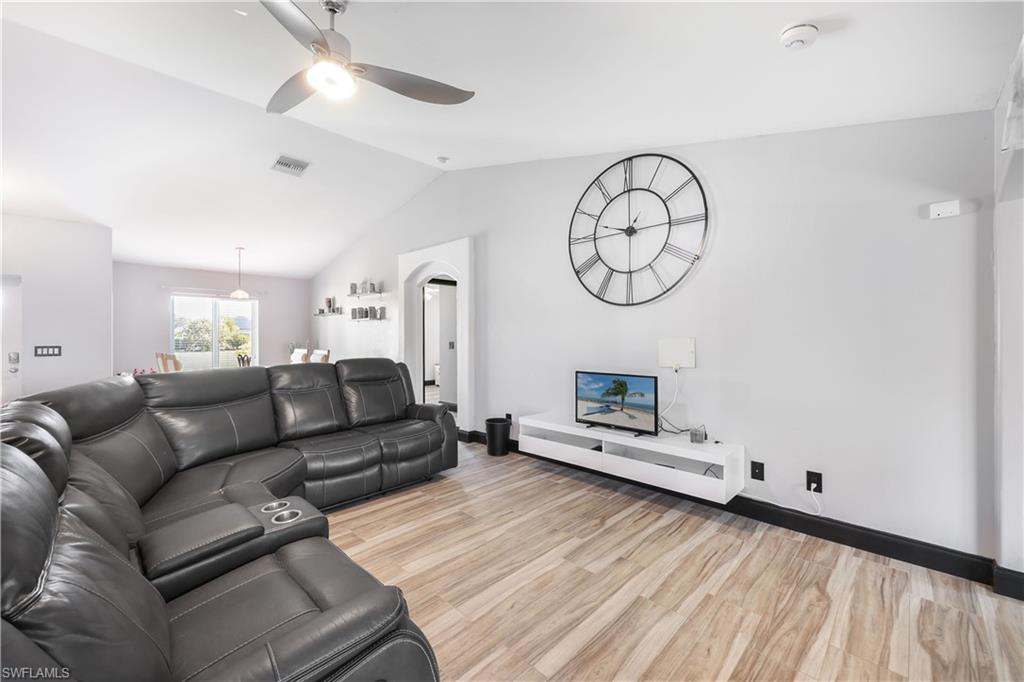 Living area with lofted ceiling, light wood finished floors, a ceiling fan, and arched walkways
