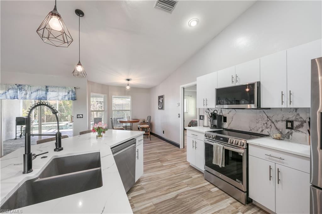 Kitchen featuring lofted ceiling, appliances with stainless steel finishes, pendant lighting, white cabinetry, and tasteful backsplash