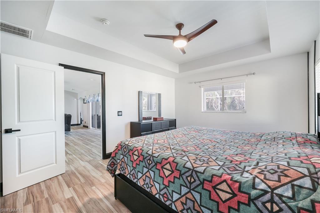Bedroom with a tray ceiling, light wood finished floors, and ceiling fan