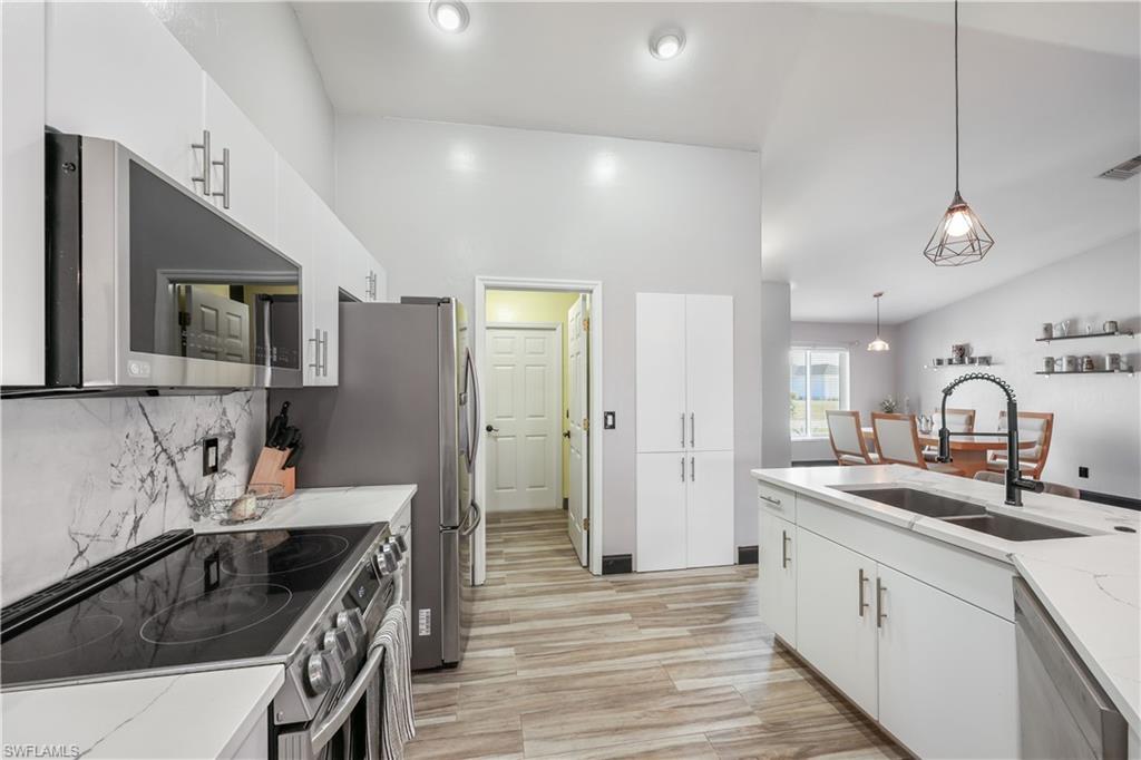 Kitchen with appliances with stainless steel finishes, pendant lighting, white cabinetry, light wood finished floors, and backsplash