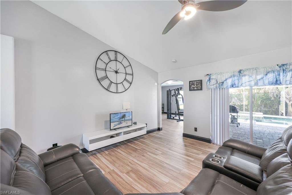 Living room featuring arched walkways, light wood-style flooring, vaulted ceiling, and ceiling fan