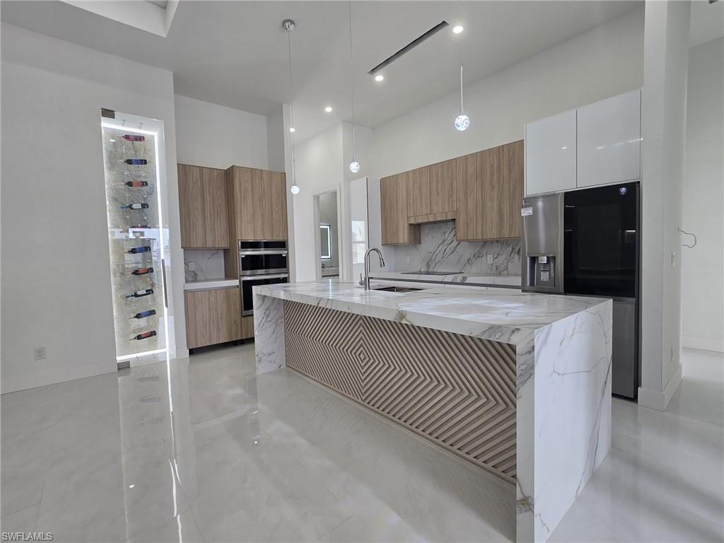 Kitchen with light stone countertops, decorative light fixtures, stainless steel appliances, tasteful backsplash, and a high ceiling