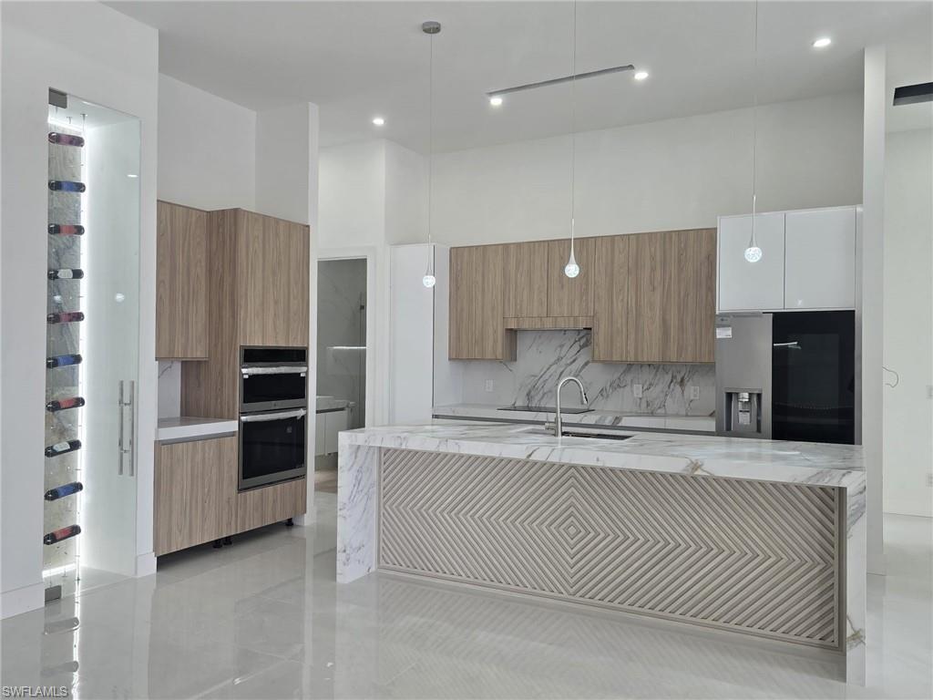 Kitchen featuring light stone counters, modern cabinets, pendant lighting, stainless steel appliances, and an island with sink