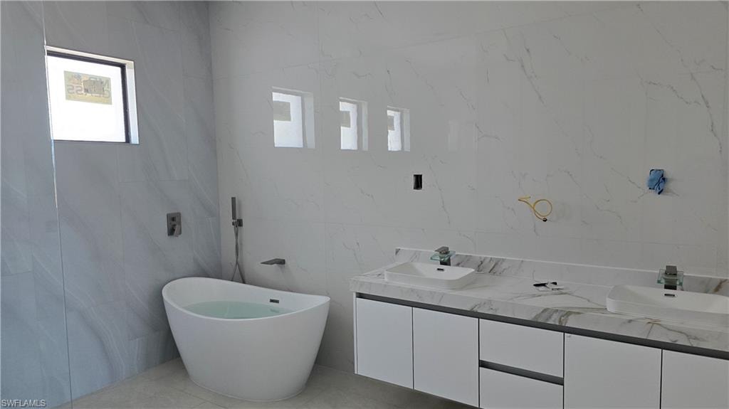 Bathroom with double vanity, a freestanding bath, and healthy amount of natural light