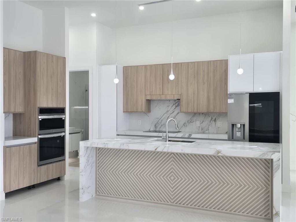 Kitchen with light stone countertops, decorative light fixtures, modern cabinets, and a high ceiling