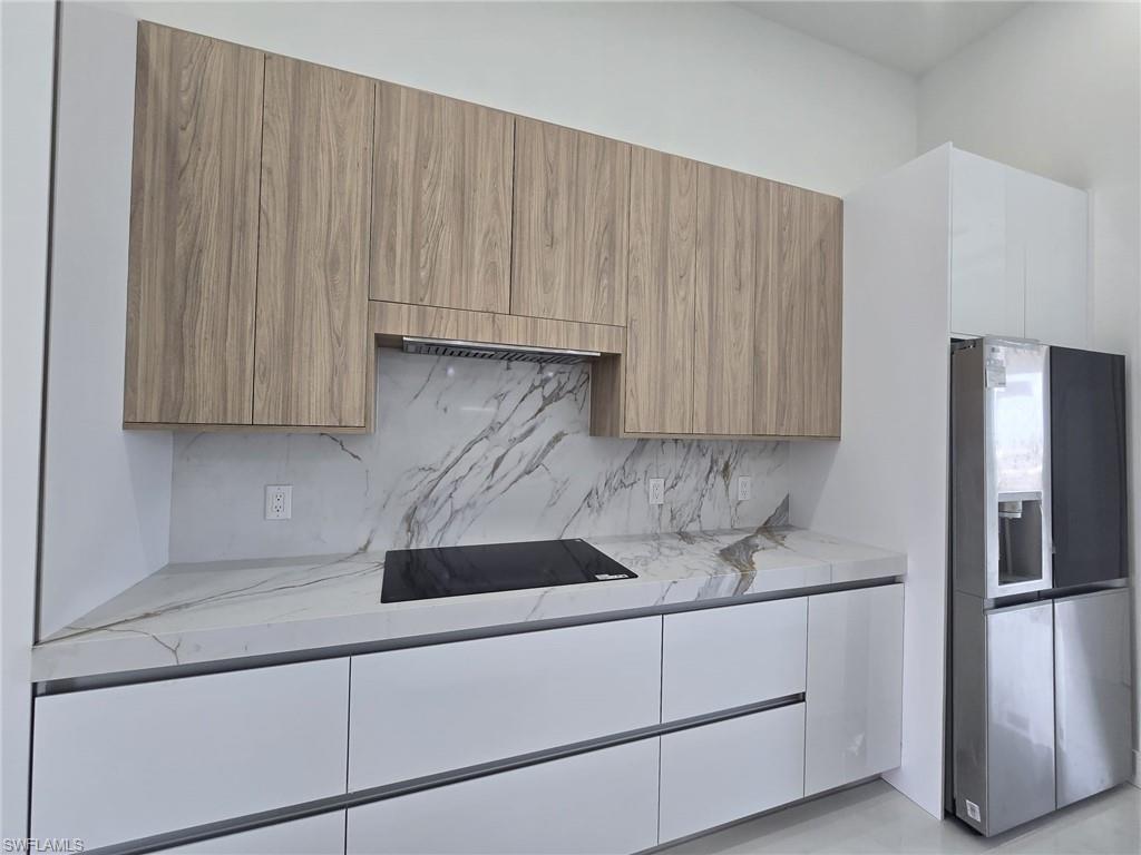 Kitchen with light stone counters, stainless steel fridge, modern cabinets, and wood finish cabinetry