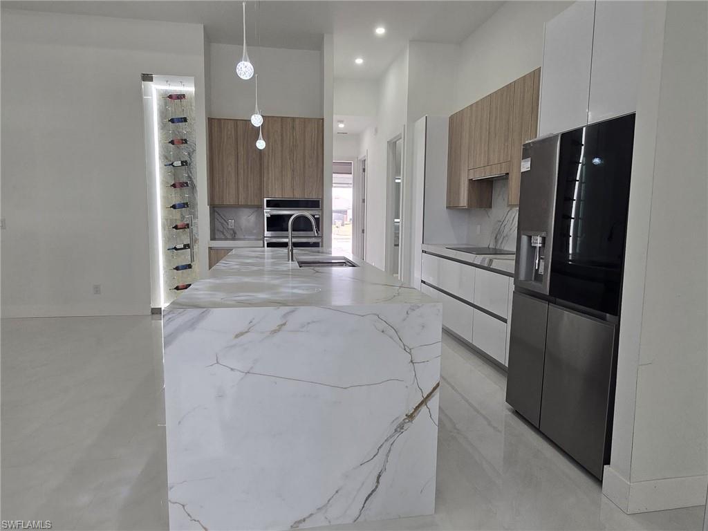 Kitchen featuring light stone counters, modern cabinets, hanging light fixtures, stainless steel appliances, and a high ceiling