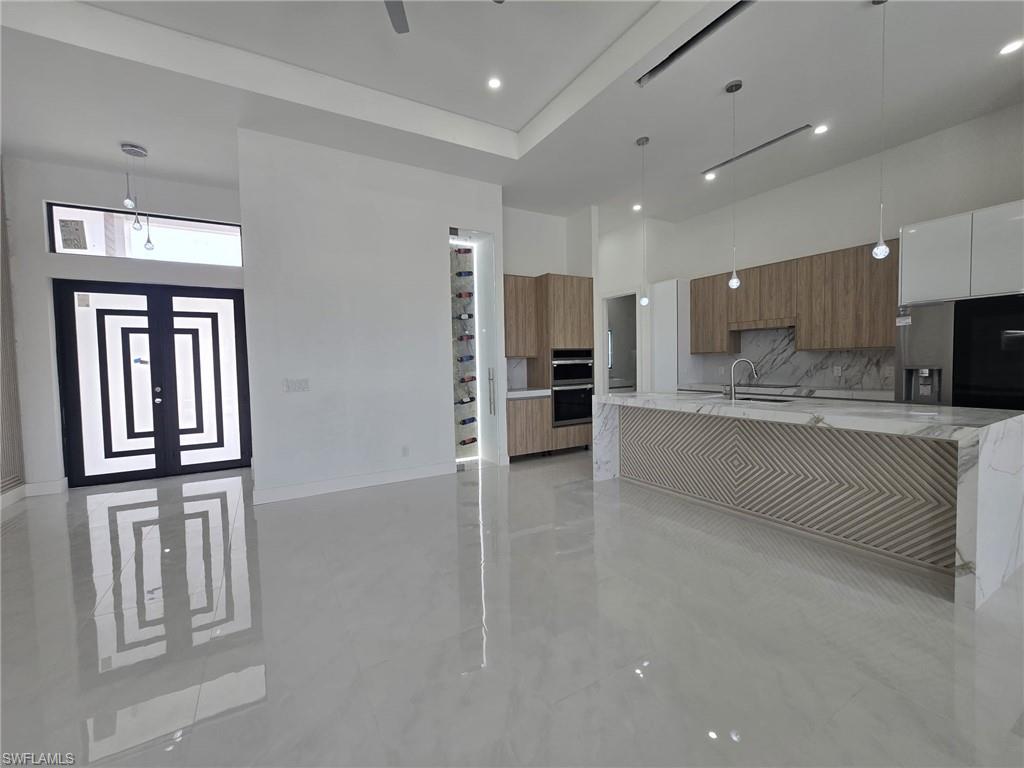 Kitchen featuring modern cabinets, light stone counters, pendant lighting, wood finish cabinets, and a high ceiling