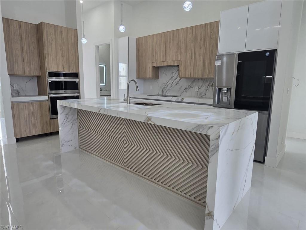 Kitchen featuring light stone countertops, wood finish cabinets, stainless steel appliances, tasteful backsplash, and a high ceiling