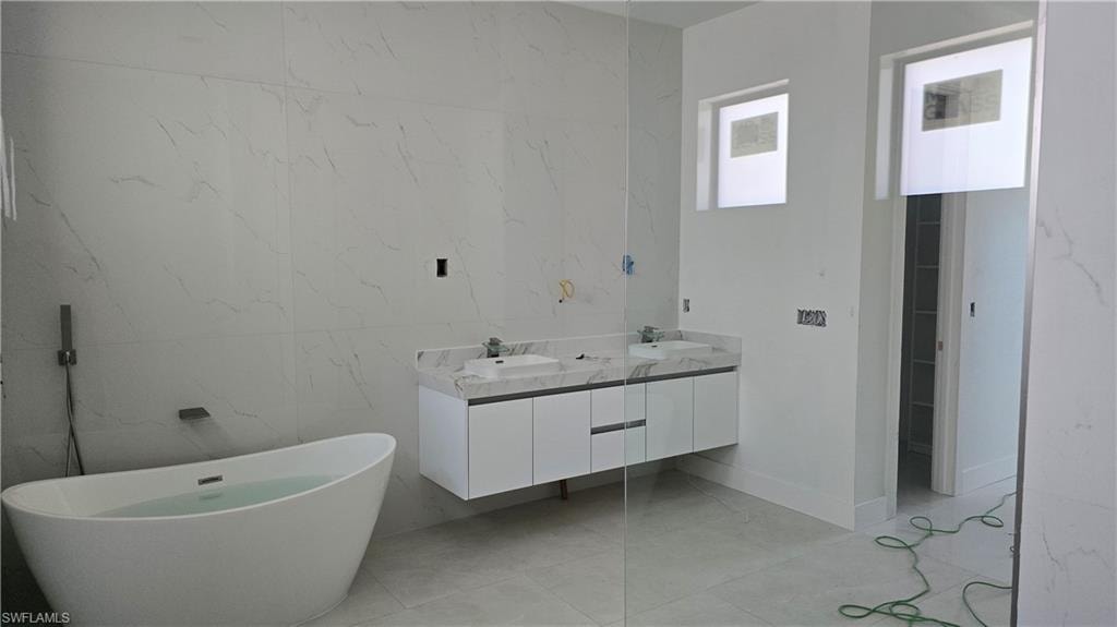Full bath with double vanity, a soaking tub, stone wall, and tile walls