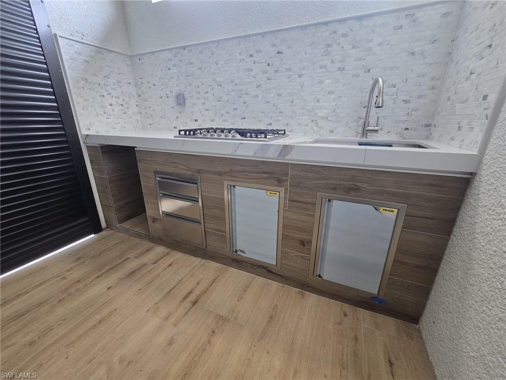 Bar area with wood finish cabinetry, modern cabinets, light wood-style floors, a textured wall, and decorative backsplash
