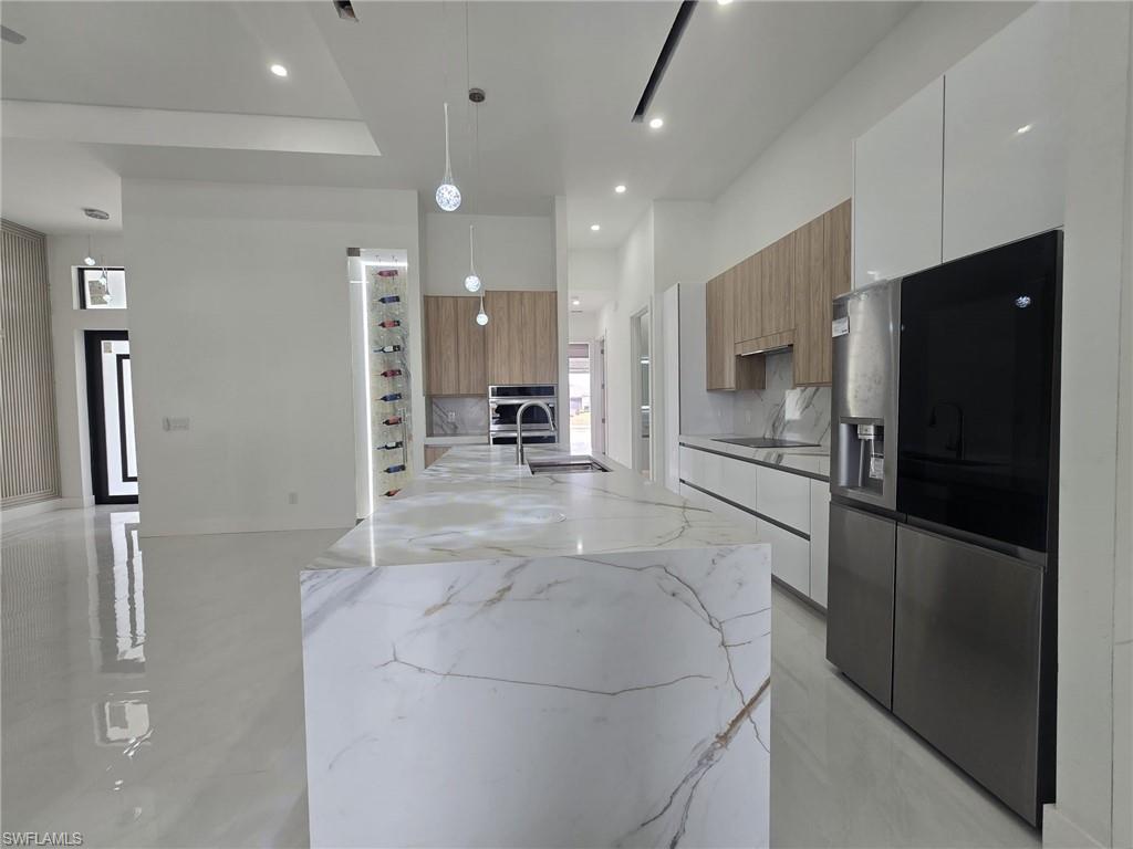 Kitchen featuring stainless steel appliances, modern cabinets, light stone countertops, and decorative light fixtures