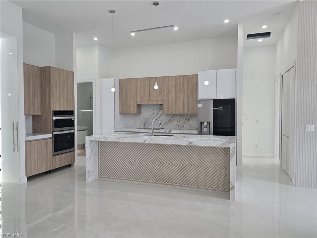 Kitchen featuring light stone countertops, modern cabinets, a center island with sink, decorative light fixtures, and a high ceiling