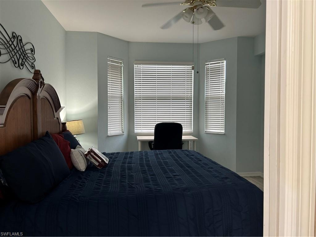 Bedroom featuring a bay window with multiple vertical windows, light blue wall paint, wood-finish flooring, and a ceiling fan